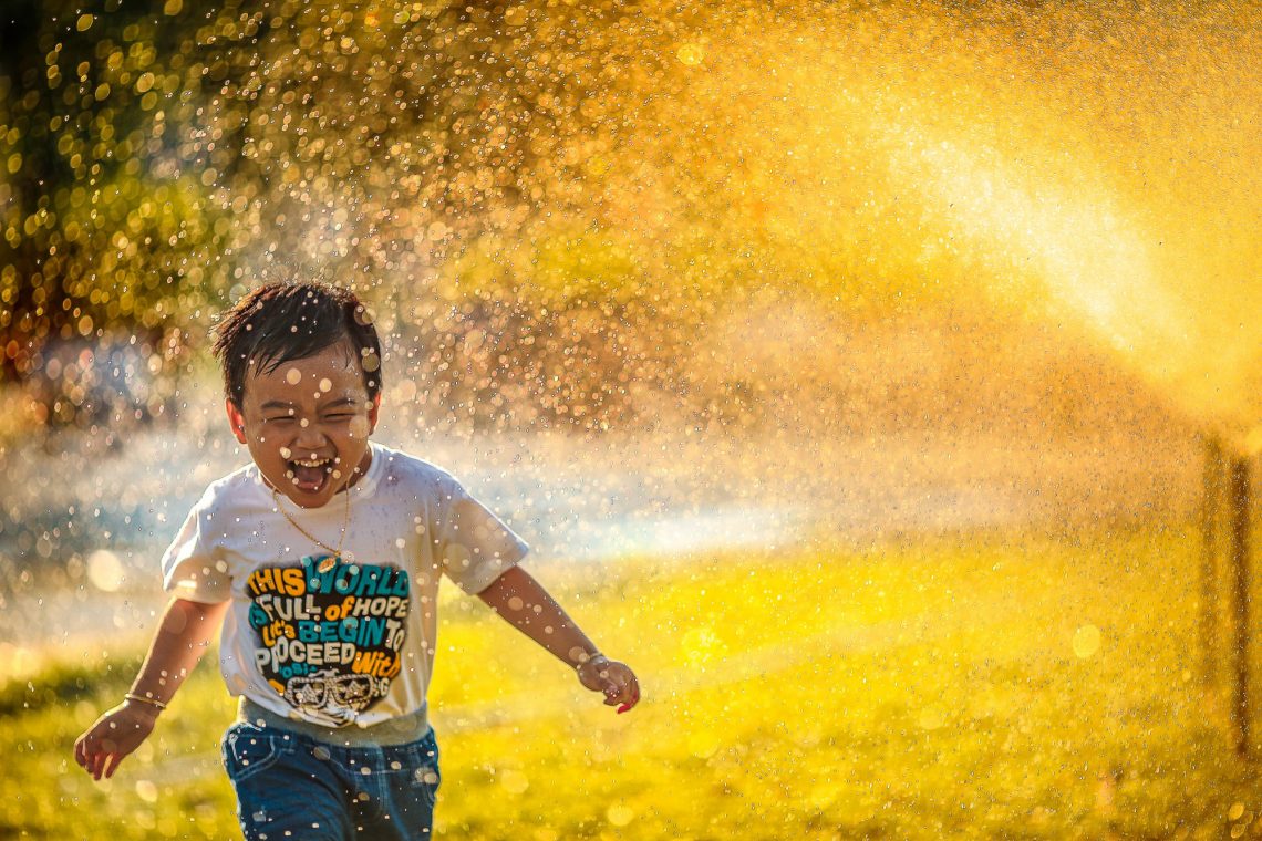 KLeiner Junge rennt durch Wasserfontaine