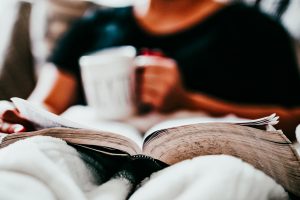 Person liest gemütlich Buch & trinkt Kaffee dabei