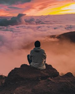 Mann sitzt auf hohem Berg und schaut auf Wolken
